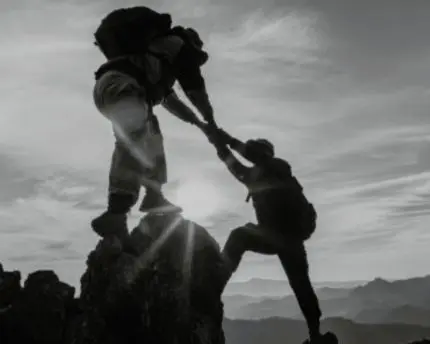 Person hiking on top of mountains helping another person below