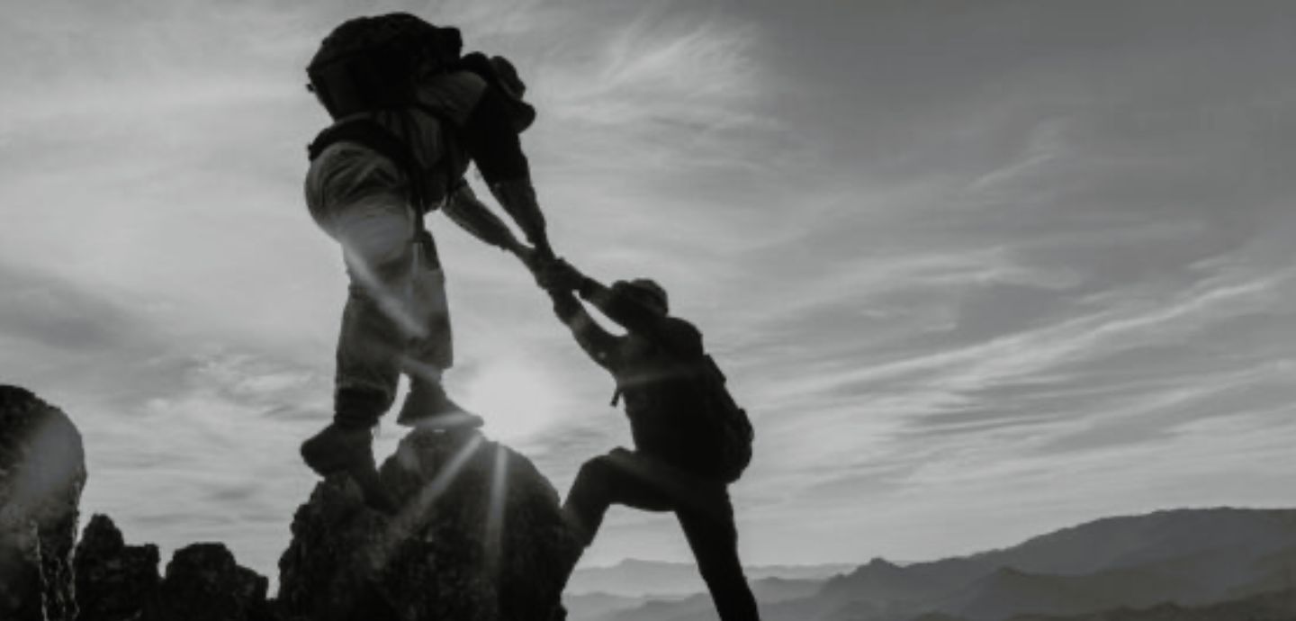 Person hiking on top of mountains helping another person below